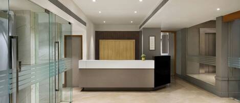 Un vestíbulo de hotel moderno con un separador de vidrio, un mostrador de recepción y un panel de pared de madera.