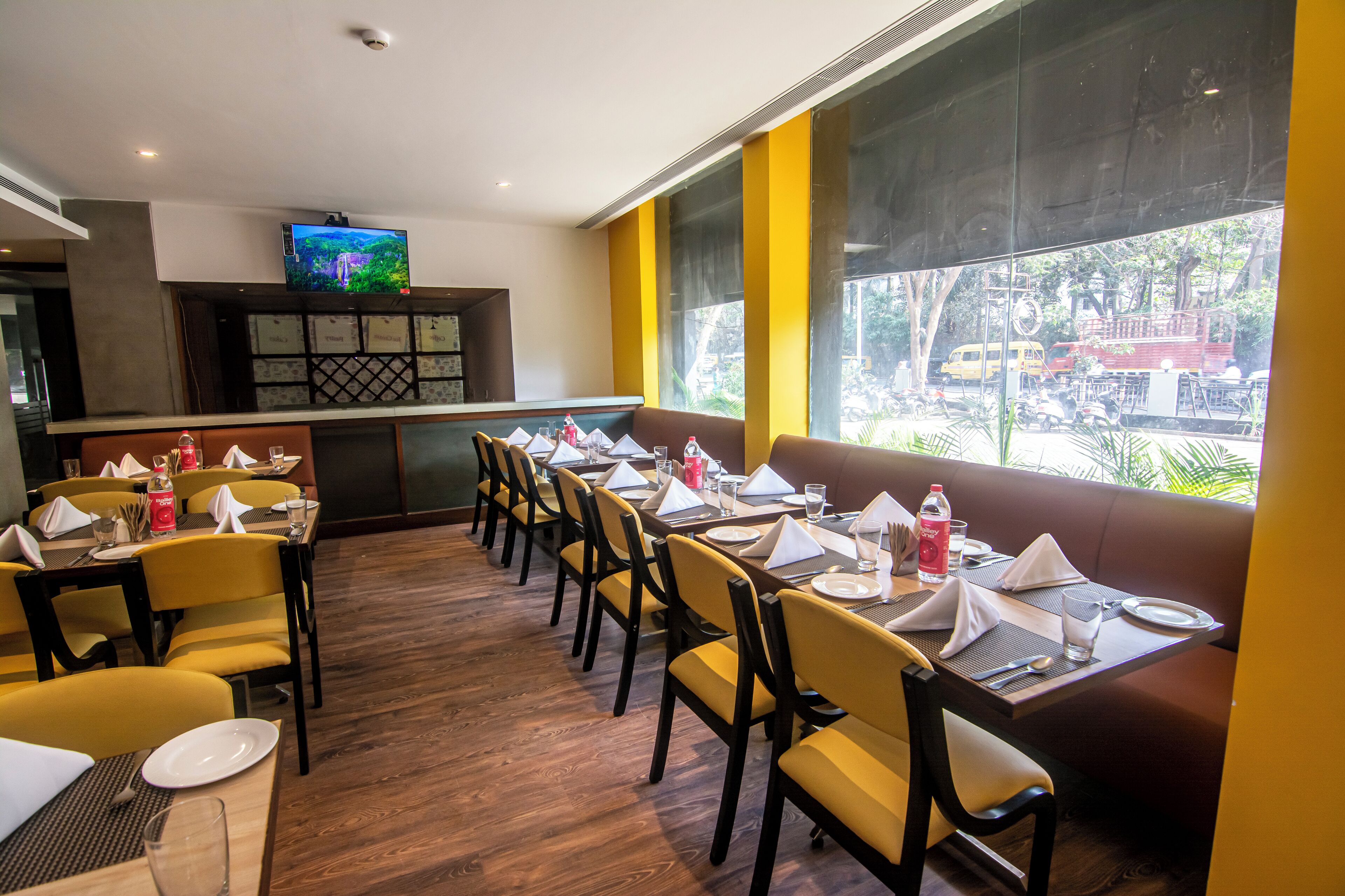Un ristorante con diversi tavoli e sedie, una televisione a parete e ampie finestre che danno su una strada.