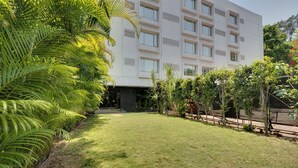 A modern building with a flat roof, large windows, and a well-maintained lawn with palm trees. - The Fern Residency Pune, Woodland, Series by Marriott (Pune)