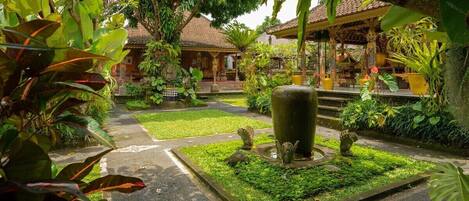 A traditional Balinese courtyard with a central water feature, surrounded by lush greenery and a tiled-roofed structure.