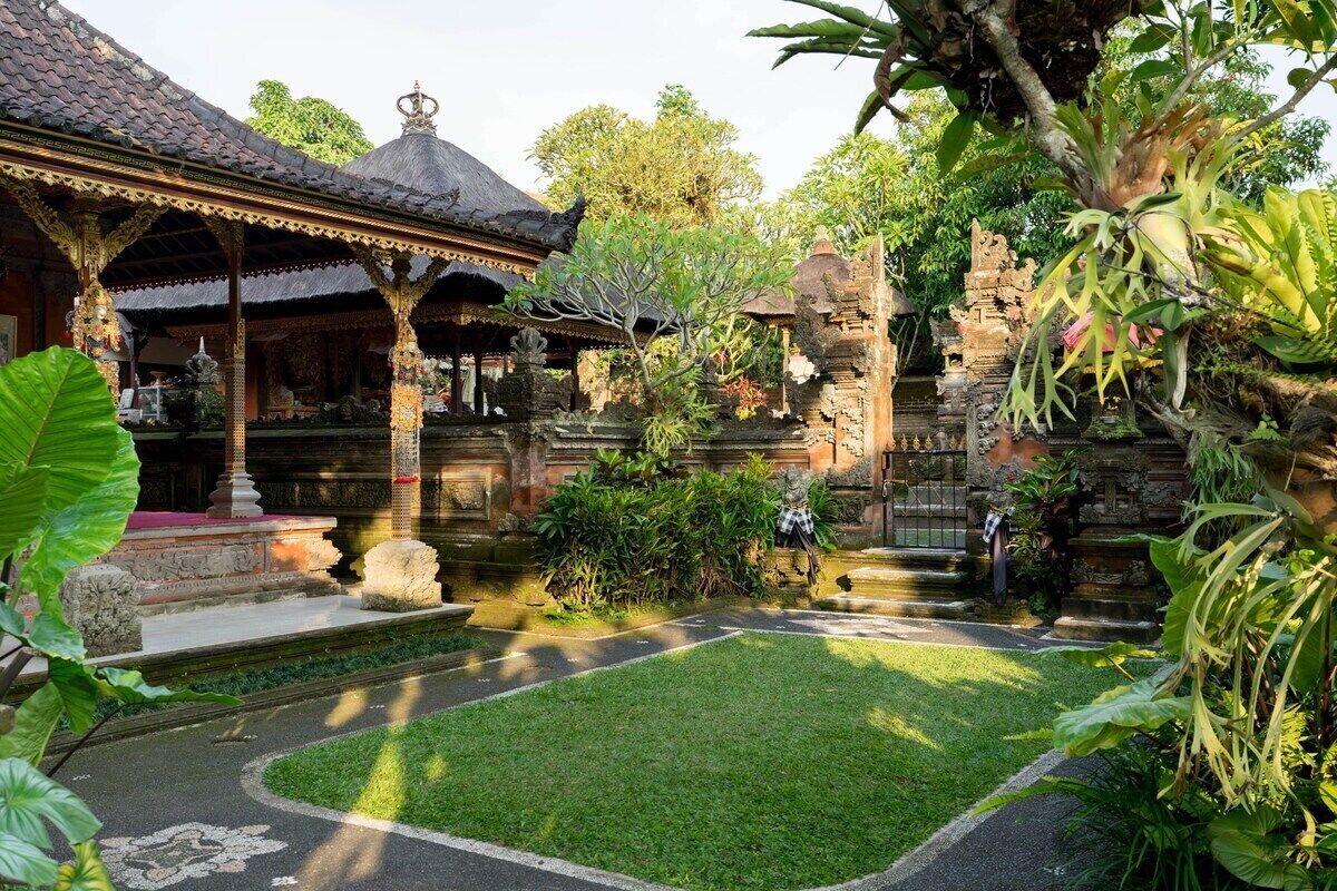 A traditional Balinese temple with a thatched roof, stone carvings, and a well-maintained garden.