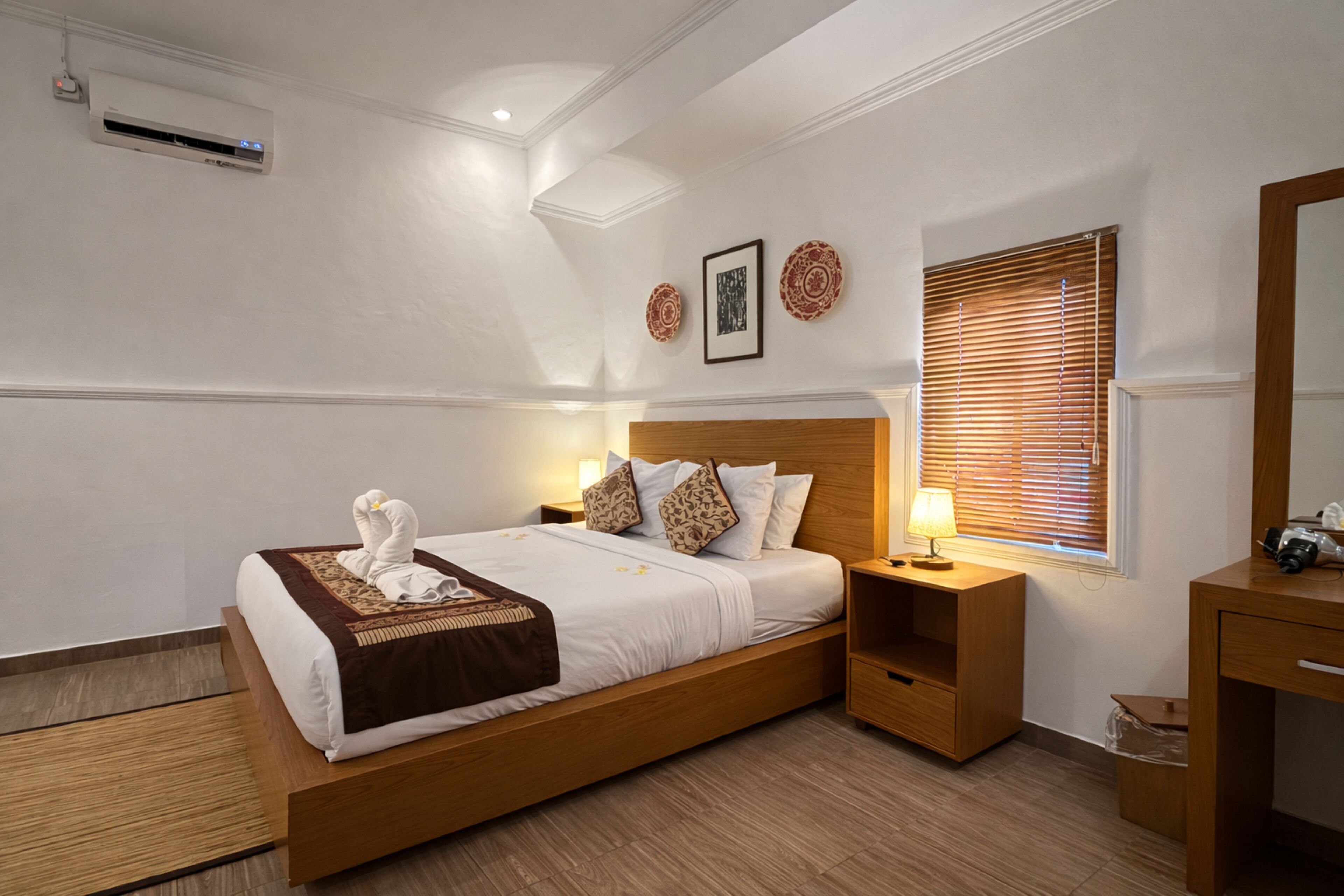 A modern hotel room with a wooden bed, bedside tables, a mirror, and a window with blinds.