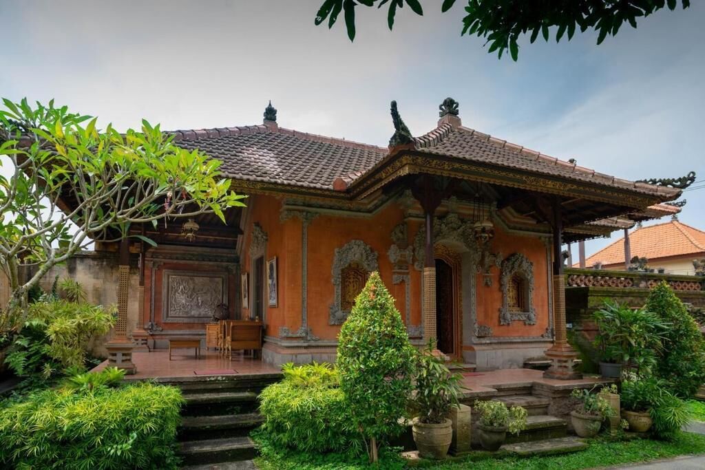 A traditional building with a tiled roof, ornate carvings, and a well-maintained garden with various plants and a staircase leading to the entrance.
