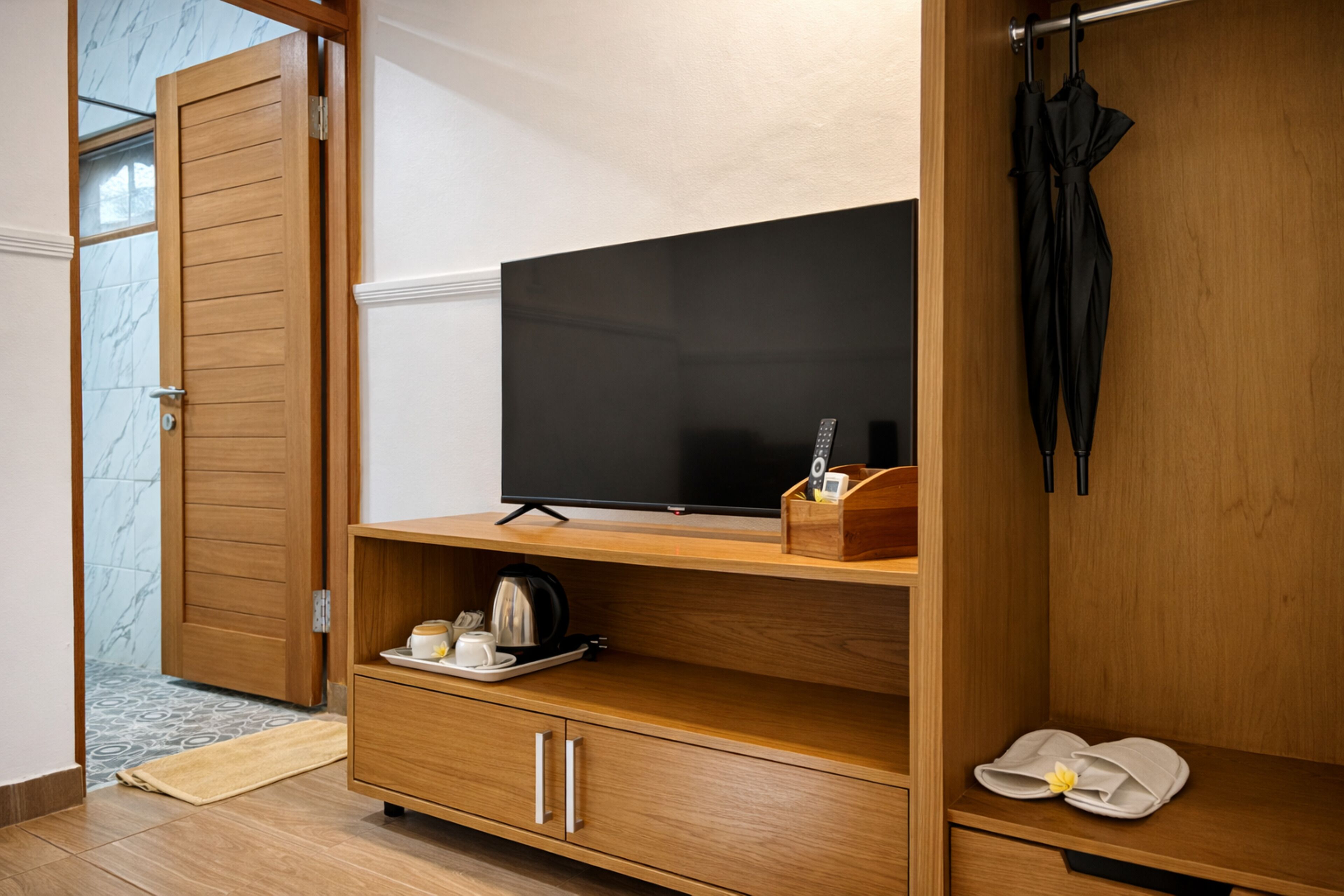 A hotel room with a wooden TV stand, a flat-screen TV, a coffee maker, and a pair of slippers on the floor.