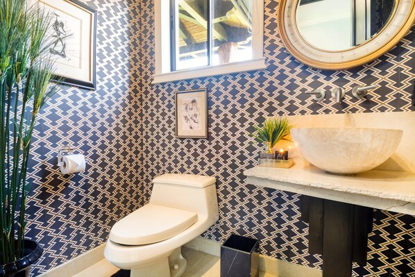 A bathroom with a patterned wall, a toilet, a sink with a large basin, and a mirror.