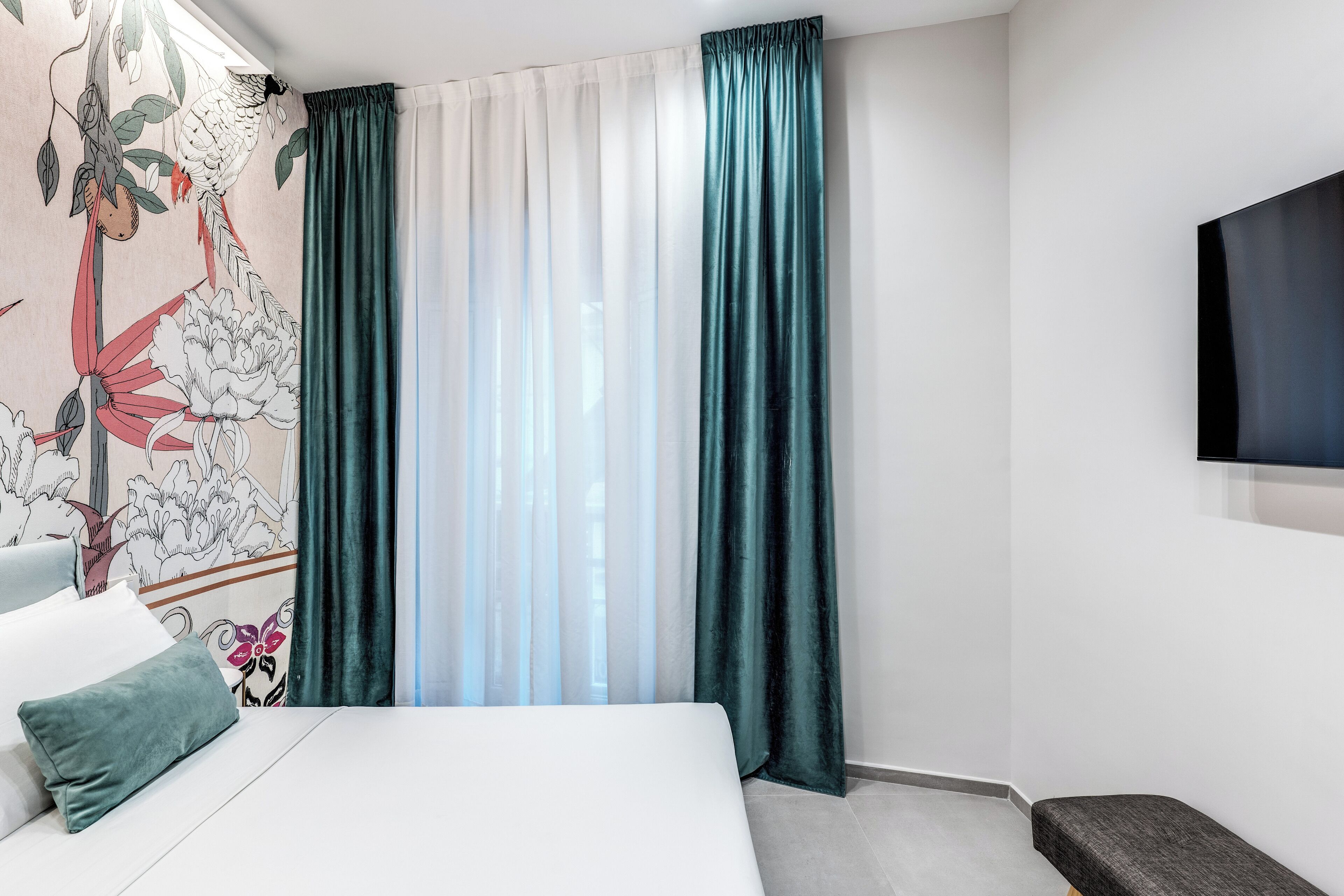 A bedroom with a bed, a bench, a TV, and curtains.
