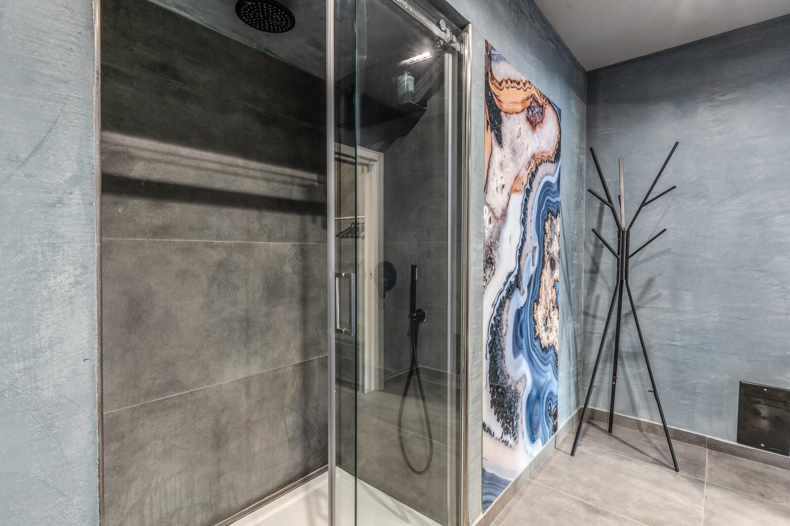 A modern bathroom with a glass-enclosed shower, a marble wall mural, and a minimalist floor lamp.