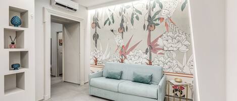 A modern living room with a light blue sofa, a decorative wall mural, and built-in shelving with decorative items.