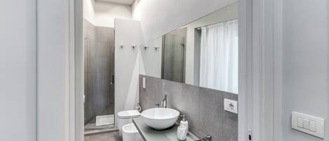 Une salle de bain moderne avec un grand miroir, un lavabo sur colonne et un espace douche.