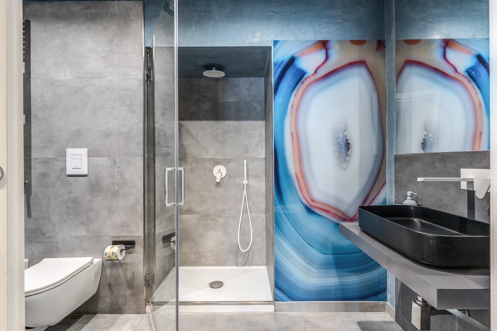 A modern bathroom with a glass-enclosed shower, a white toilet, and a black sink.