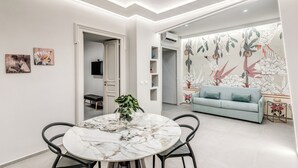 A modern living room with a light blue sofa, a round marble table with chairs, and a floral wallpaper. - Lady Diamond (Naples)