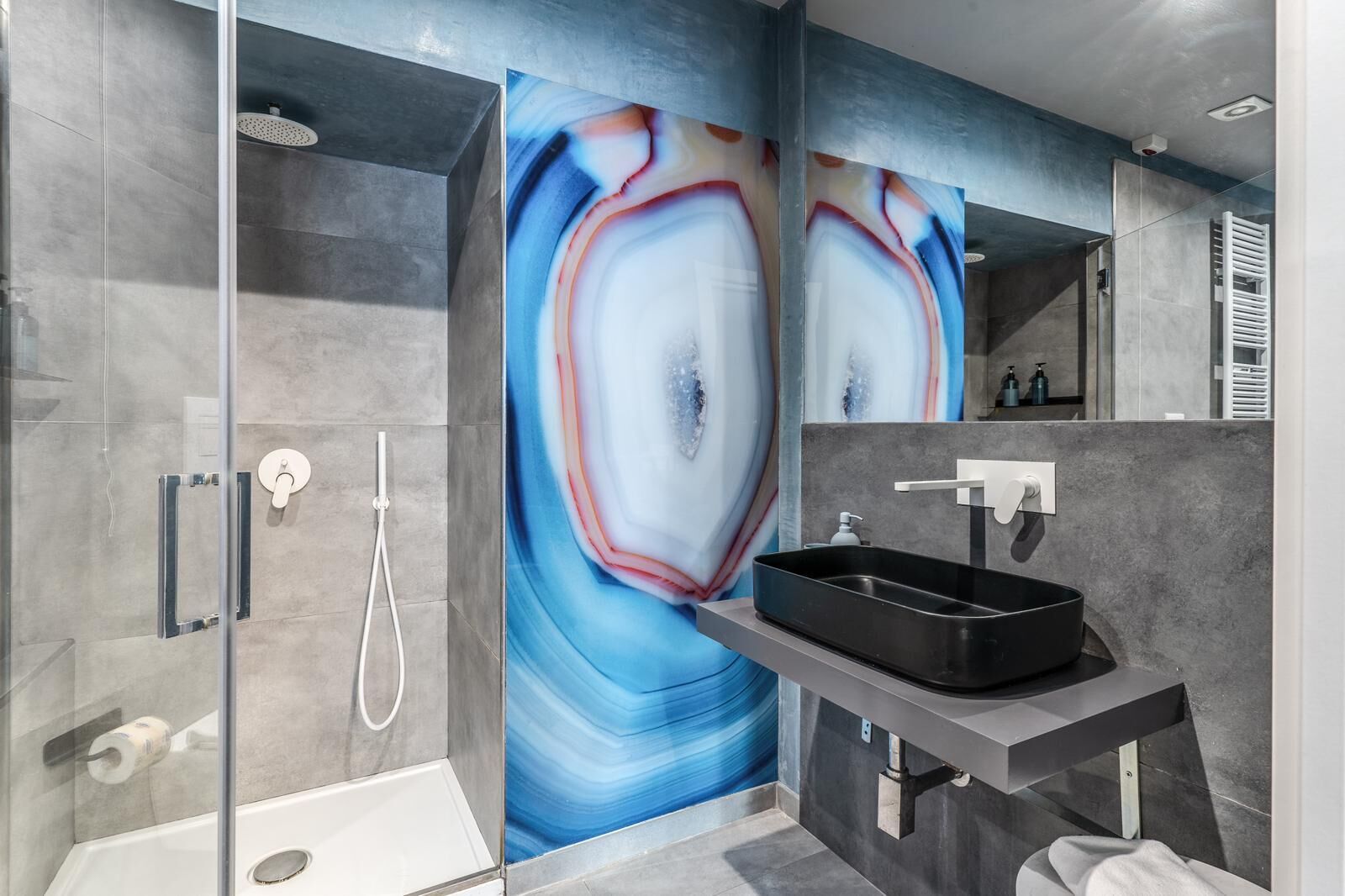 A modern bathroom with a glass-enclosed shower, a black sink, and a large abstract mural on the wall.