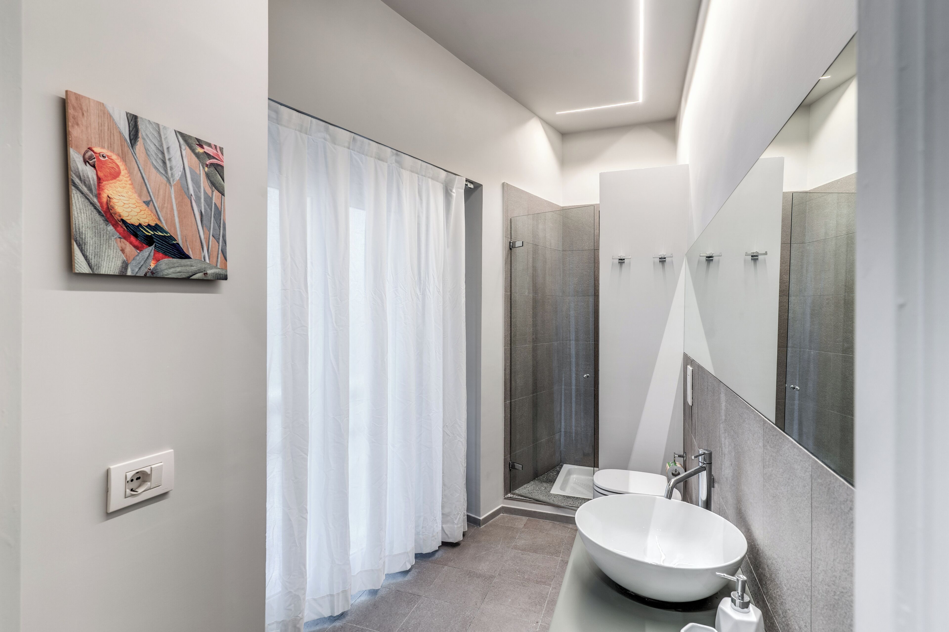 Un baño moderno con un espejo grande, un lavamanos blanco y una zona de ducha.