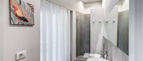 Un baño moderno con un espejo grande, un lavamanos blanco y una zona de ducha.