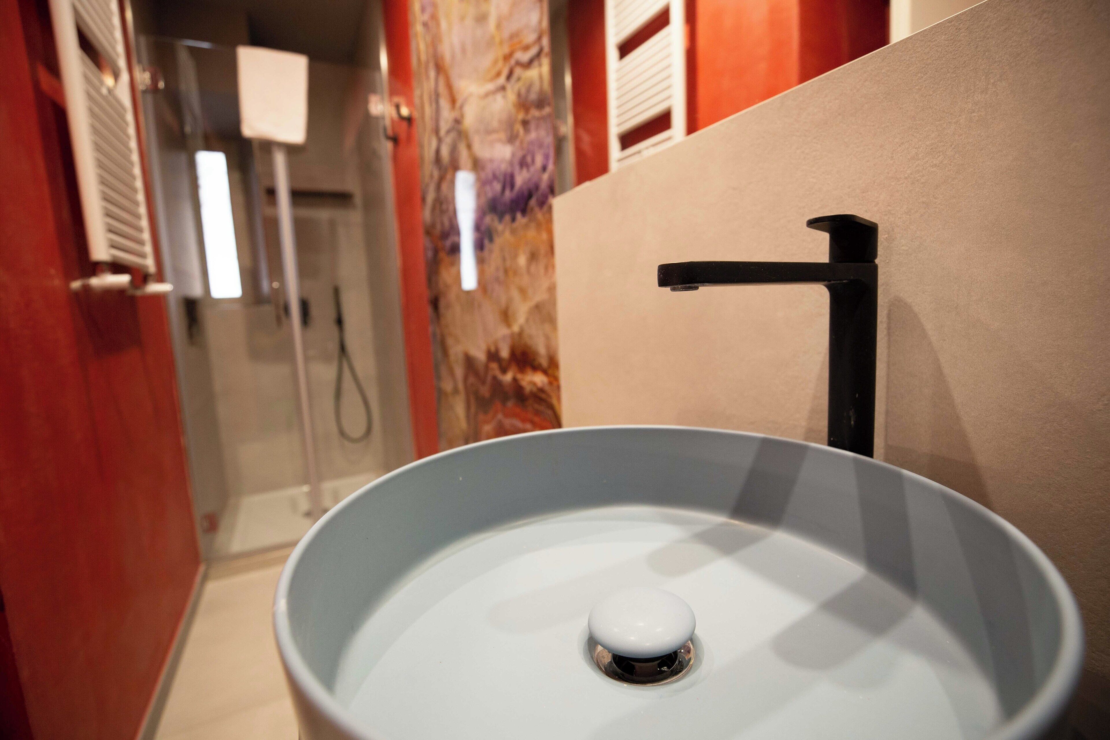 Un baño con un lavamanos blanco, una ducha y una pared roja.