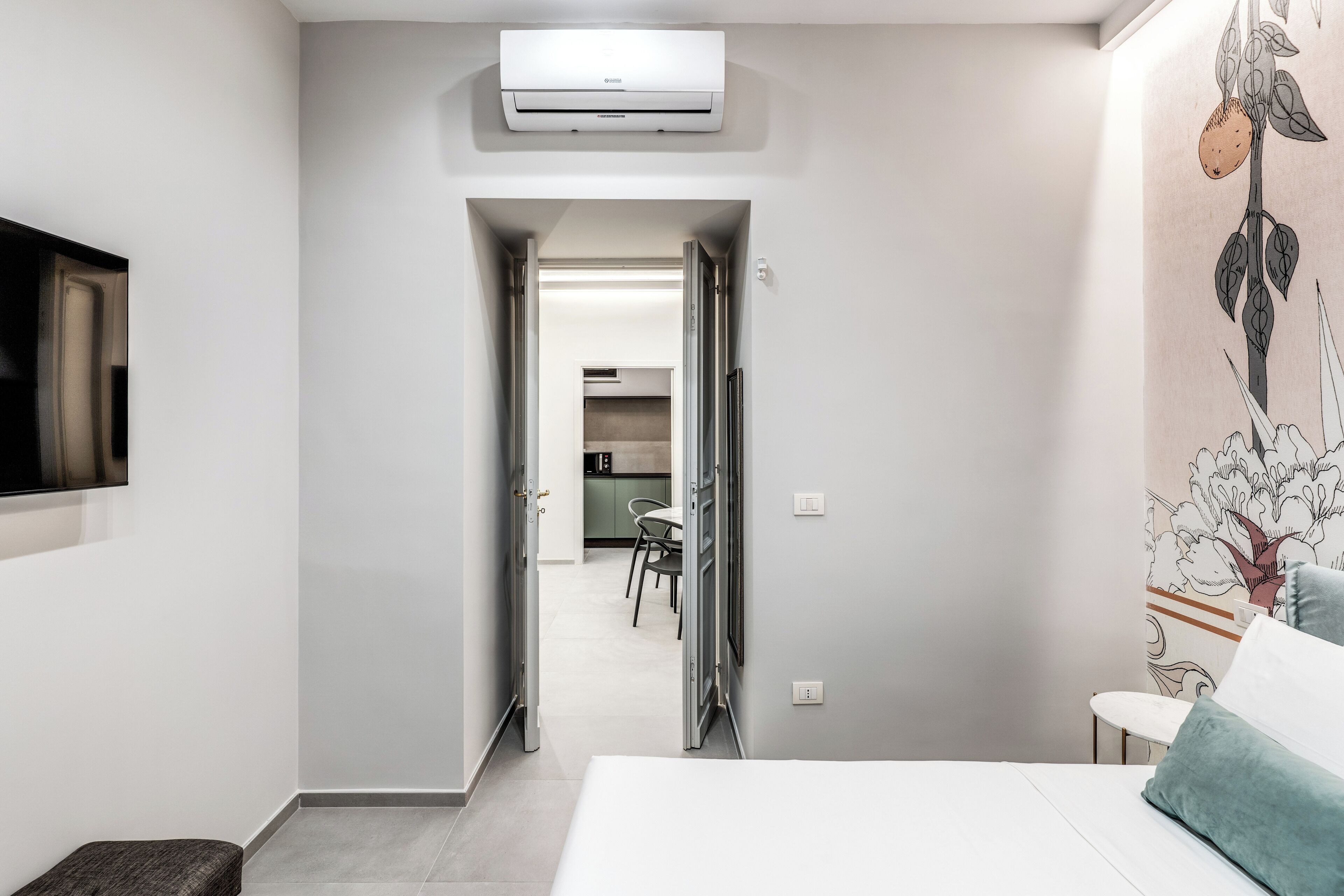 Een moderne hotelkamer met een bed, een televisie en een kitchenette op de achtergrond.