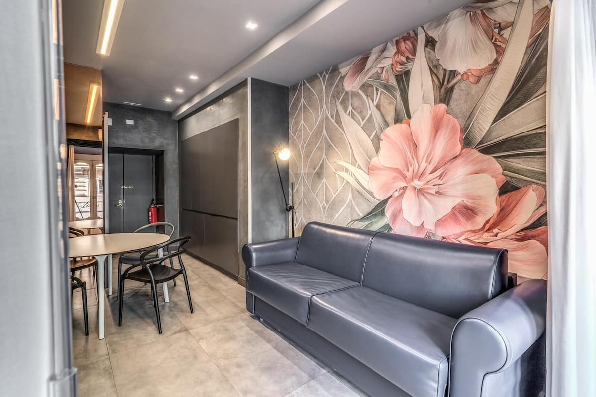Un salon moderne avec un canapé, une table à manger et des chaises, ainsi qu’une grande fresque florale sur le mur.