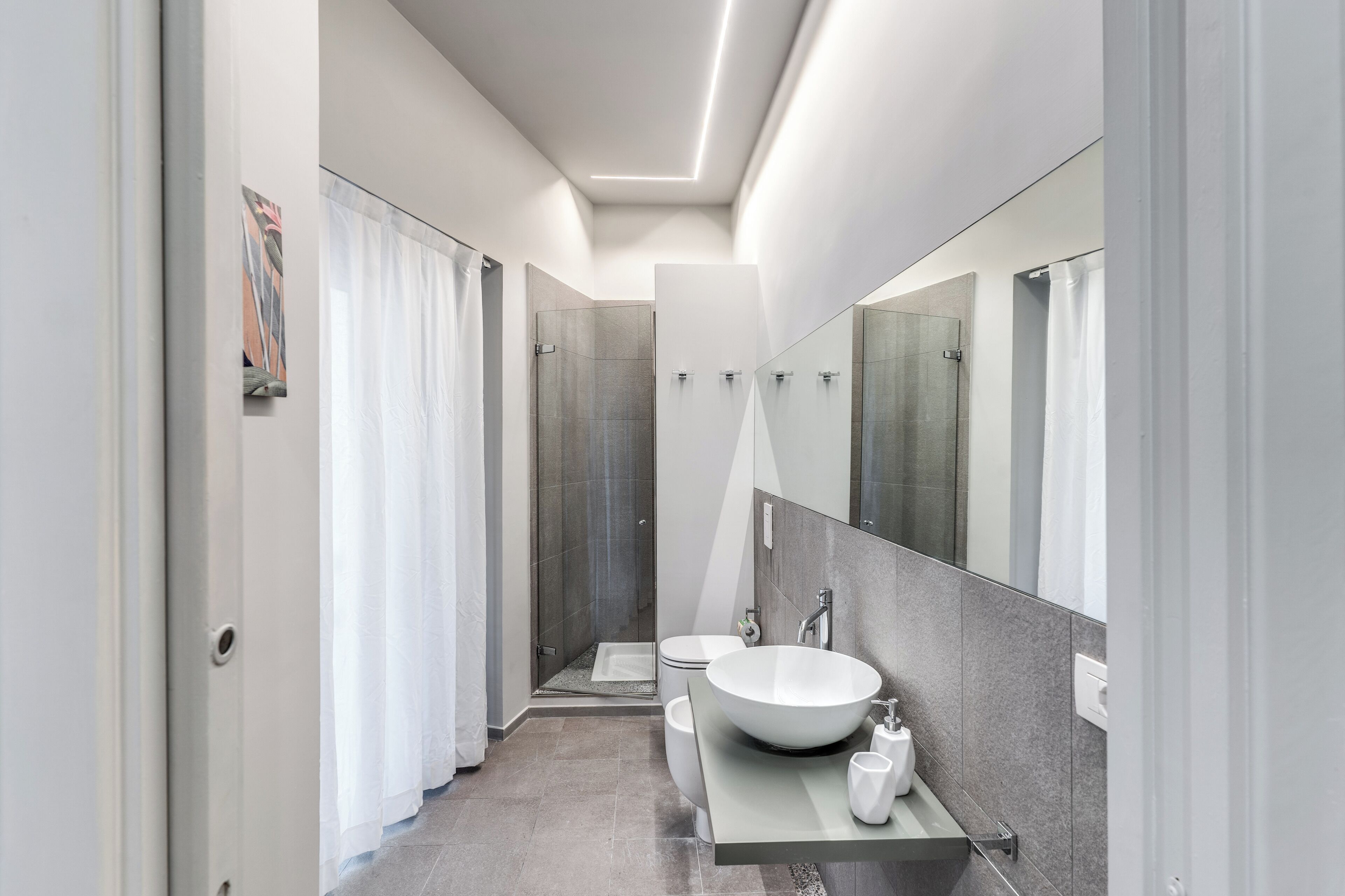 Une salle de bain moderne avec un grand miroir, un lavabo sur colonne et un espace douche.