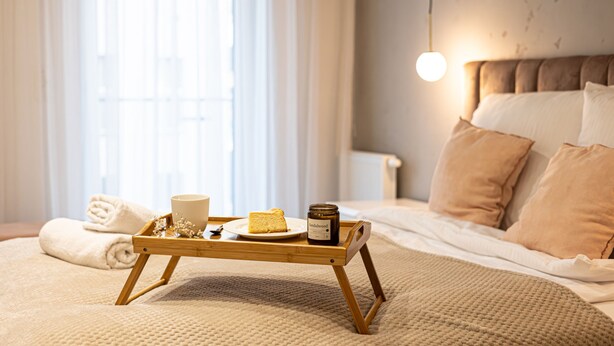 Una cama bien hecha con una bandeja de madera que sostiene un plato de comida, un frasco y una taza.