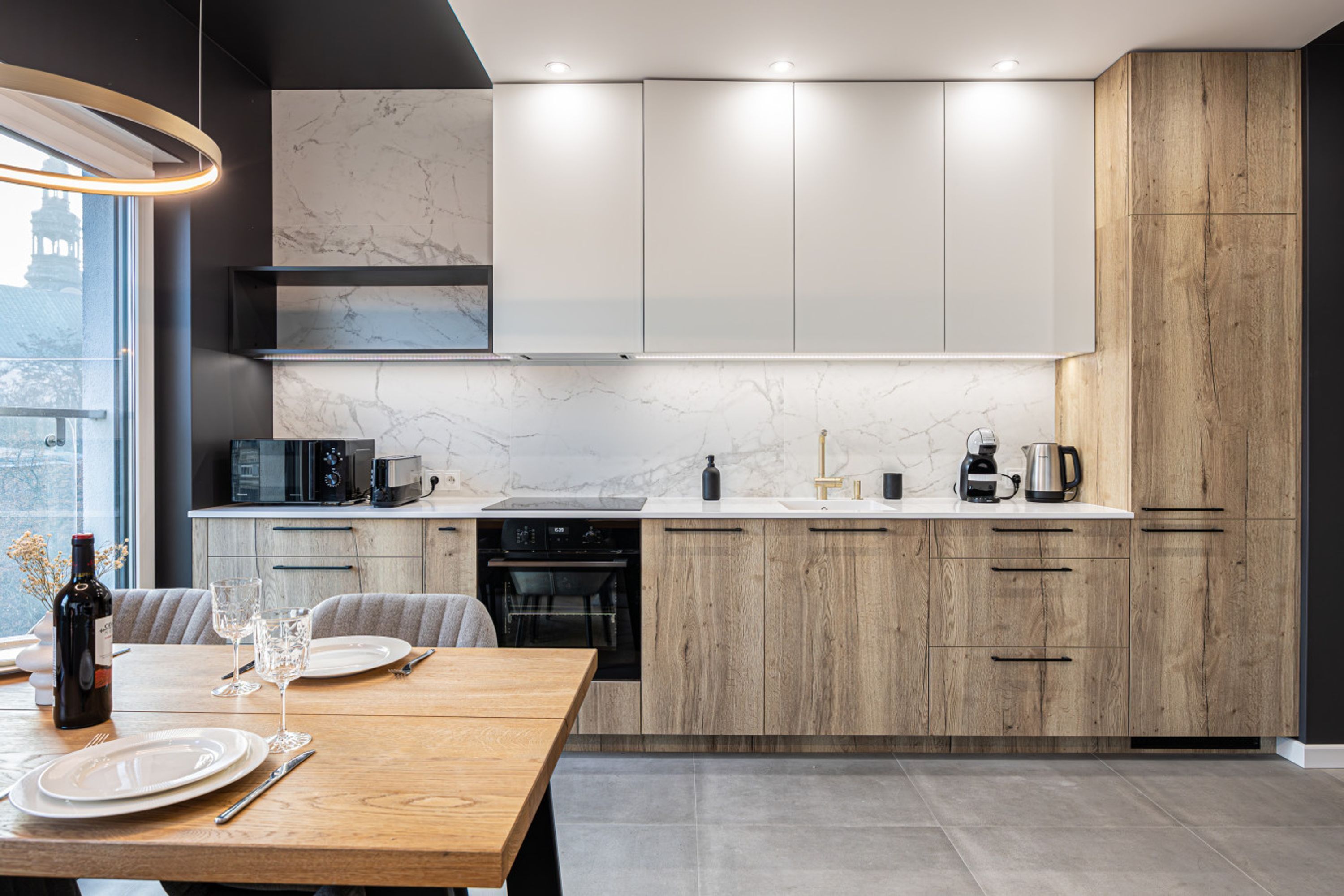 Una cocina moderna con armarios de madera, un salpicadero de mármol y un comedor con una mesa de madera preparada para dos personas.