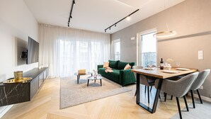 Una sala de estar moderna con un sofá verde, una mesa de comedor con sillas y un televisor de pantalla plana montado en la pared.