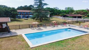 A rectangular swimming pool with lounge chairs and umbrellas, surrounded by a fenced area with a grassy lawn and trees. - DOMAINE DU FLAMAND - BRUYÈRE (Naujac-sur-Mer)