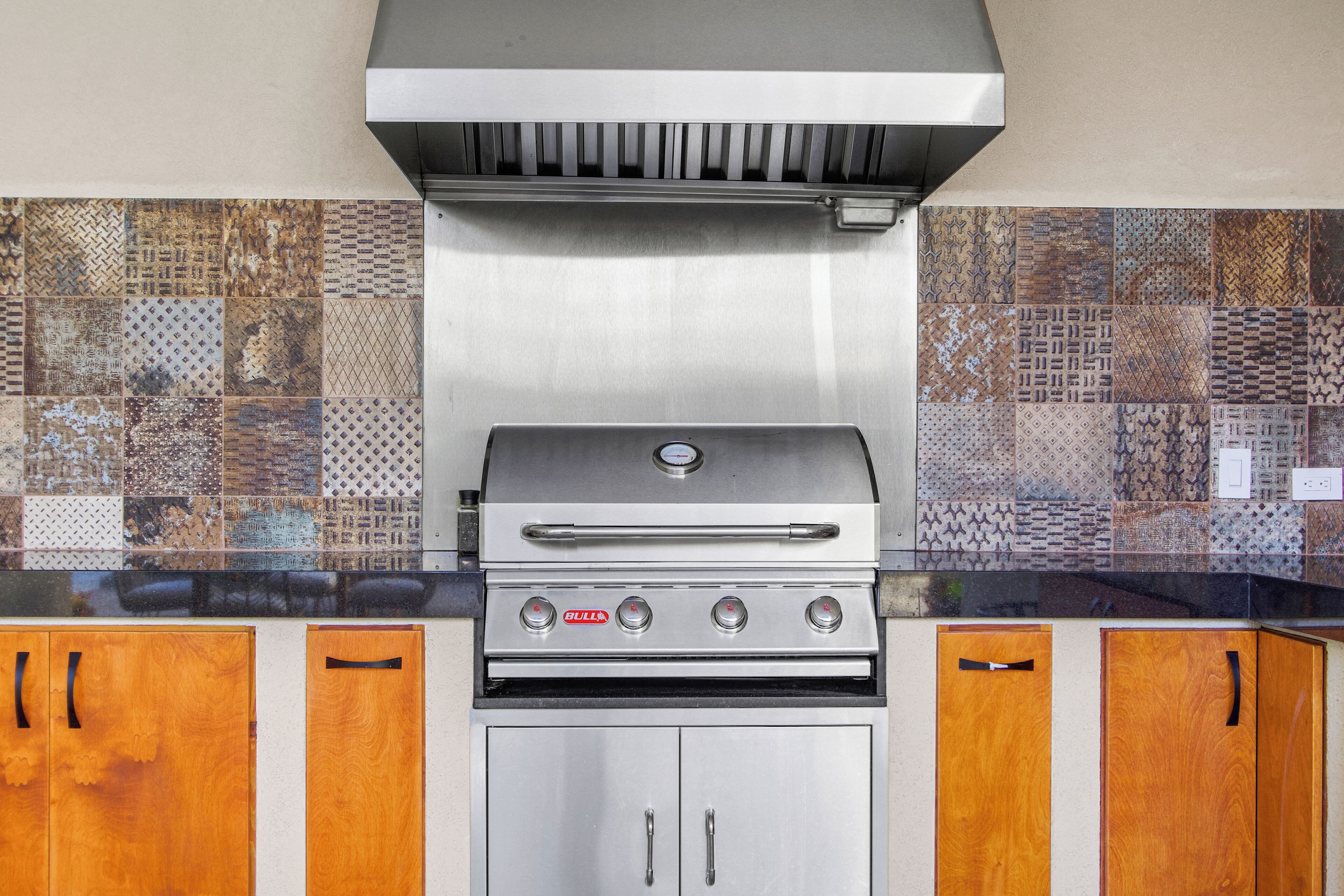 A stainless steel grill with a digital display, wooden cabinets, and a patterned backsplash.