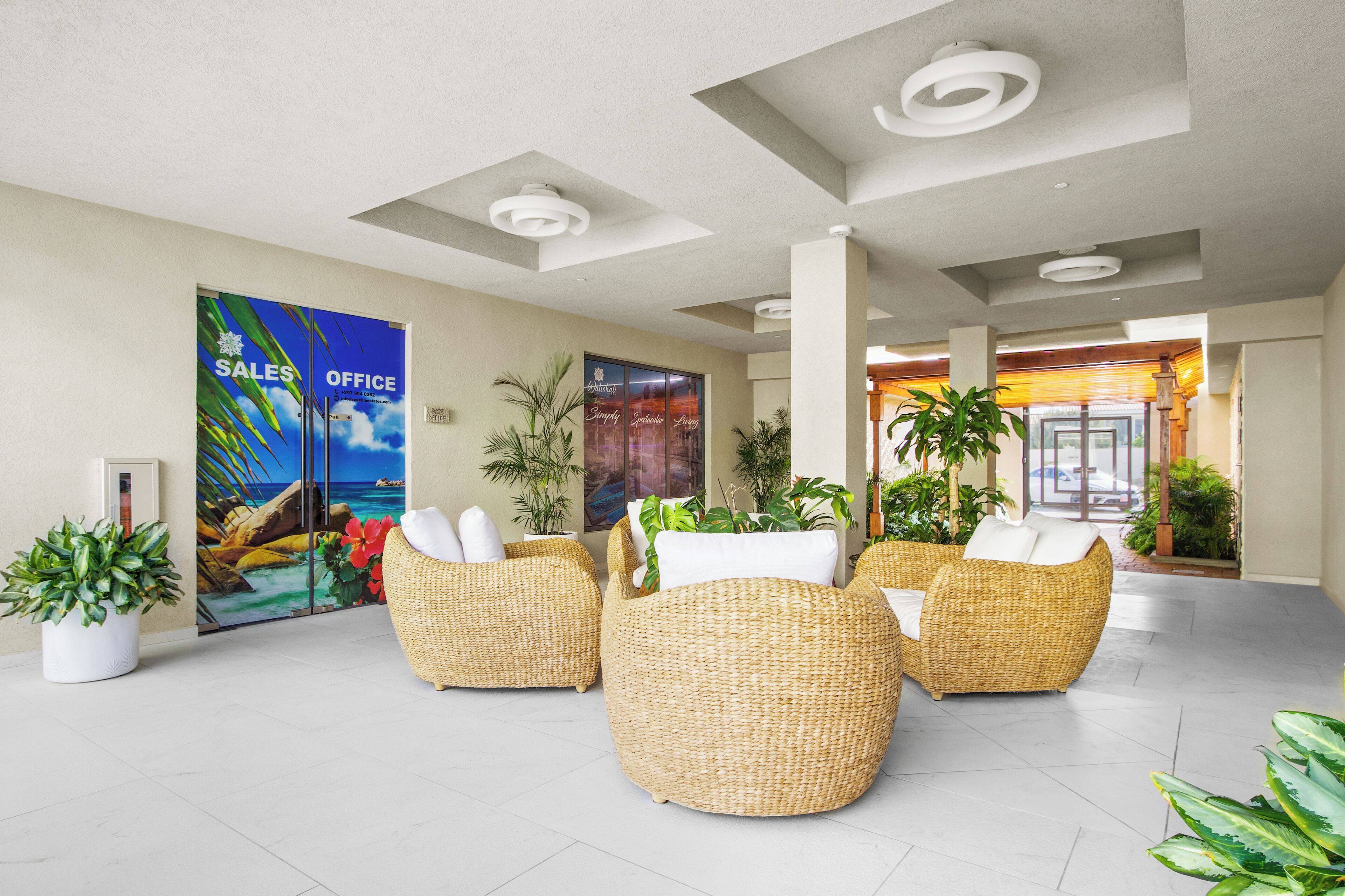 A spacious lobby with wicker sofas, potted plants, and a 'Sales Office' sign.