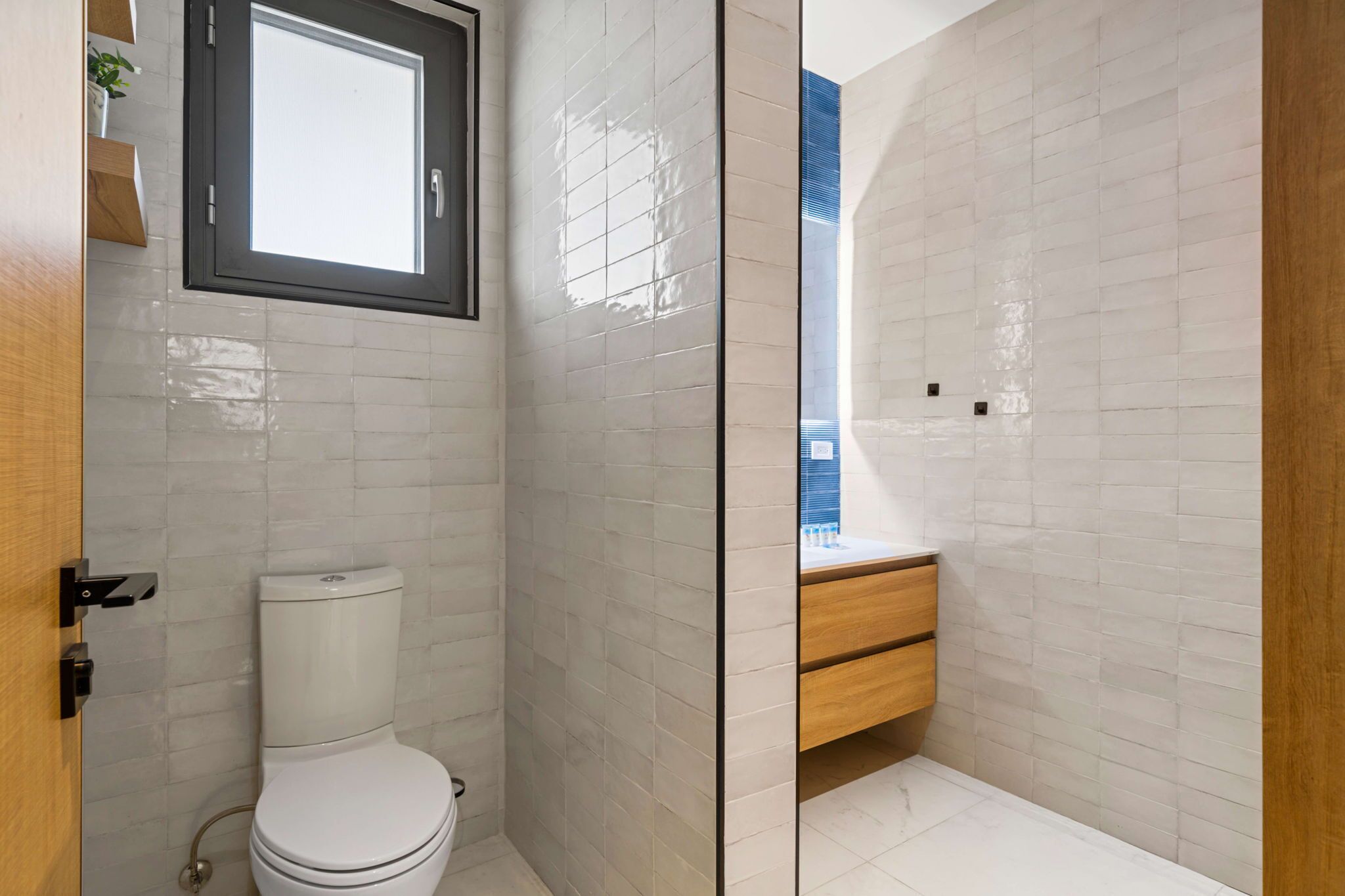 Een badkamer met toilet, raam en houten wastafelmeubel.