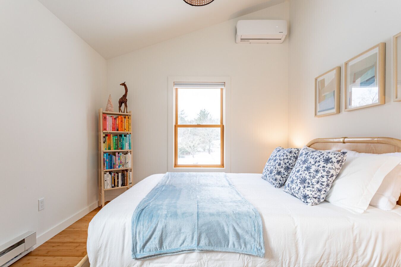 A bedroom with a bed, a bookshelf, a window, and an air conditioner.