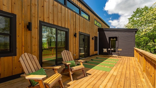 A wooden deck with Adirondack chairs and a small table, overlooking a garden. - Chic Home w/ Fireplace & Beautiful Sunsets (Callicoon)