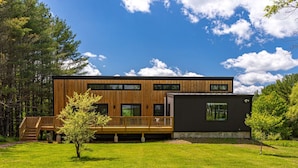 A modern wooden house with a deck, large windows, and a separate black section. - Chic Home w/ Fireplace & Beautiful Sunsets (Callicoon)