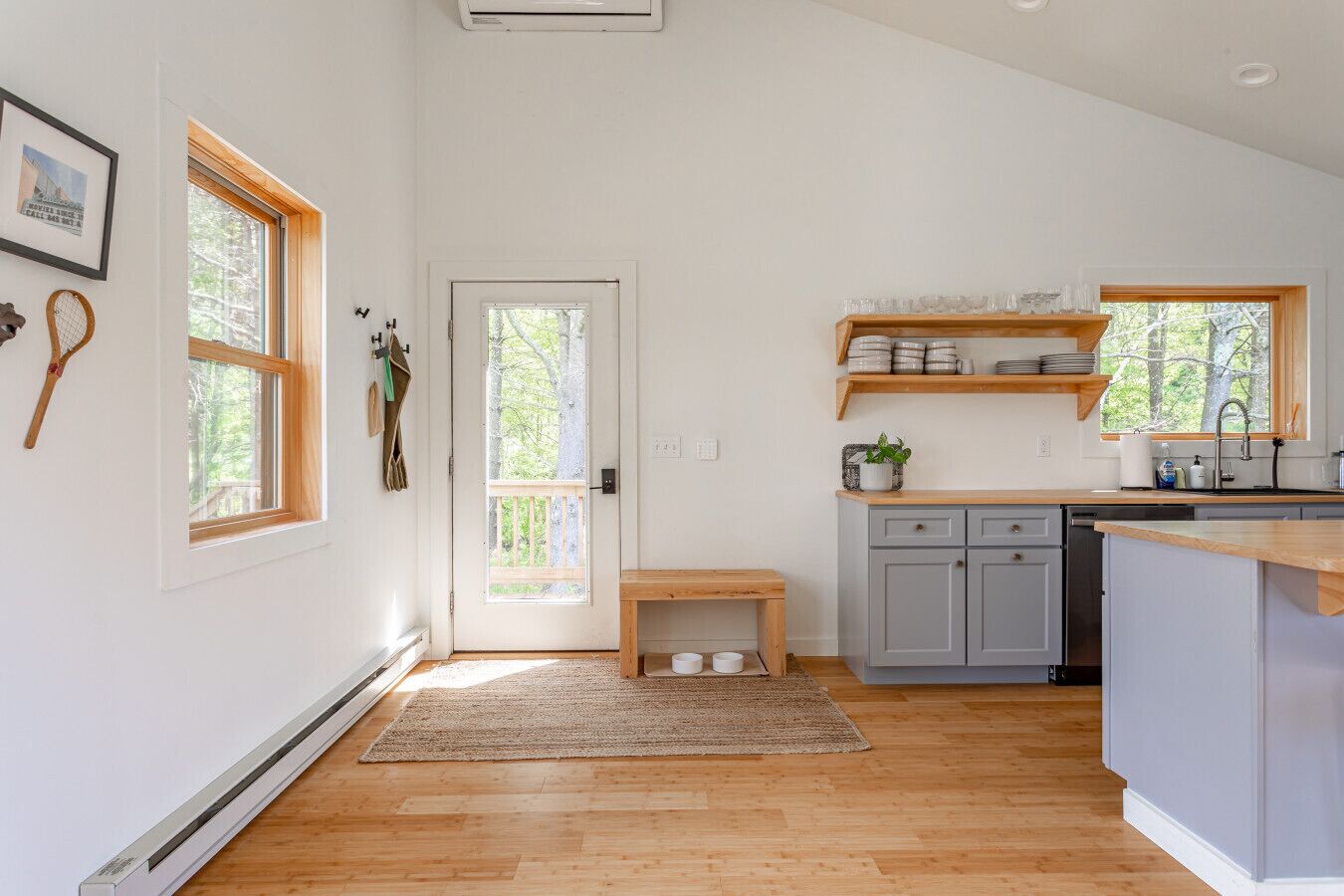 Een moderne keuken met houten vloeren, een inbouwvaatwasser en een klein houten bankje.