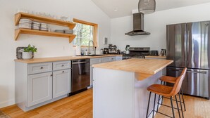 A modern kitchen with a central island, stainless steel appliances, and wooden shelves. - Chic Home w/ Fireplace & Beautiful Sunsets (Callicoon)