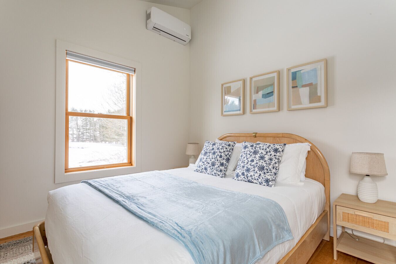 A bedroom with a bed, a window, a bedside table, and a wall-mounted air conditioner.