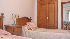 A bedroom with two single beds, wooden wardrobes, a bedside table with a lamp, and a mirror on the wall. - Casa Ana           . (Conil de la Frontera)