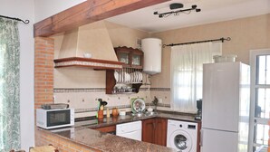 A kitchen with a brick wall, a microwave, a washing machine, and a refrigerator. - Casa Ana           . (Conil de la Frontera)