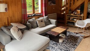 A cozy wooden cabin interior with a sofa, a coffee table, a white chair, and a staircase. - Apartment With Parking in Chatel (Chatel)