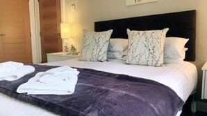 A neatly made bed with a purple blanket, two pillows with a floral pattern, and two folded white towels on the bed. - Overlooking Carlingford Lough Modern and Spacious! (Warrenpoint)