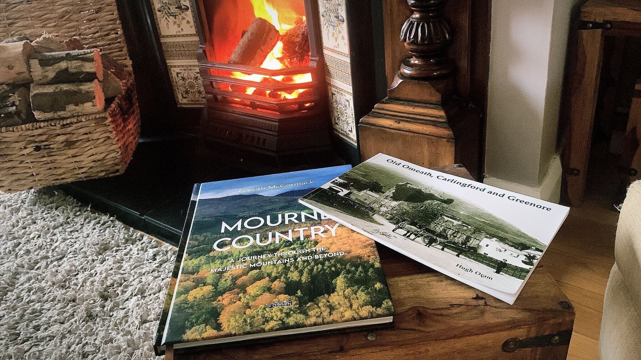 A book titled 'MOURN COUNTRY' by Gareth McCormack on a wooden table next to a fireplace with a visible fire.