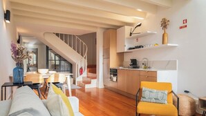 A modern living space with a staircase leading to a loft bedroom, a kitchen with white cabinets, and a dining area with wooden furniture.