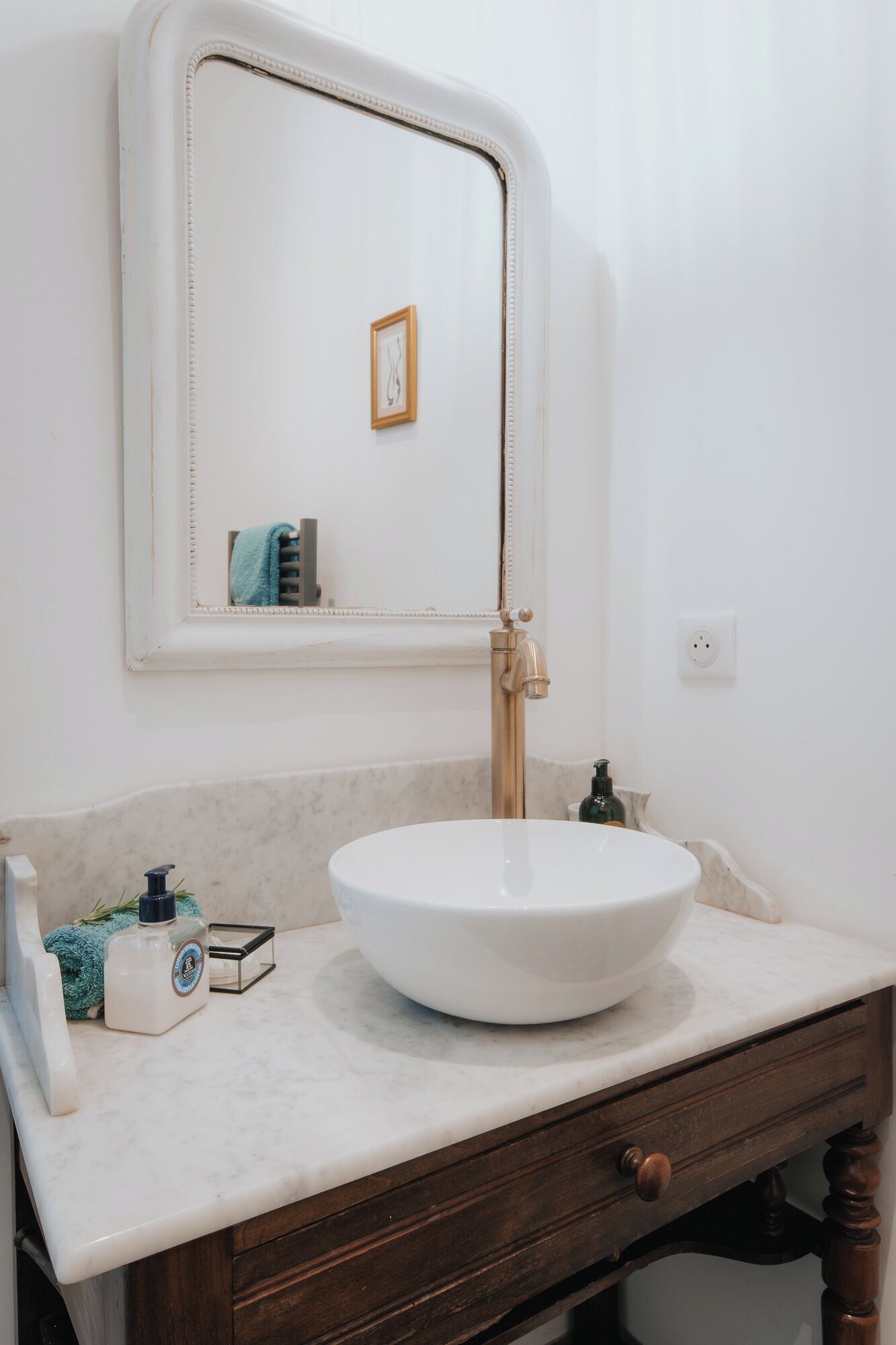 Een badkamer met een witte wastafel, een gouden kraan, een spiegel en een houten opbergmeubel.