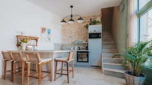 Cozinha com bancada branca, cadeiras de madeira, luminária pendente, micro-ondas e escada que dá para uma varanda.