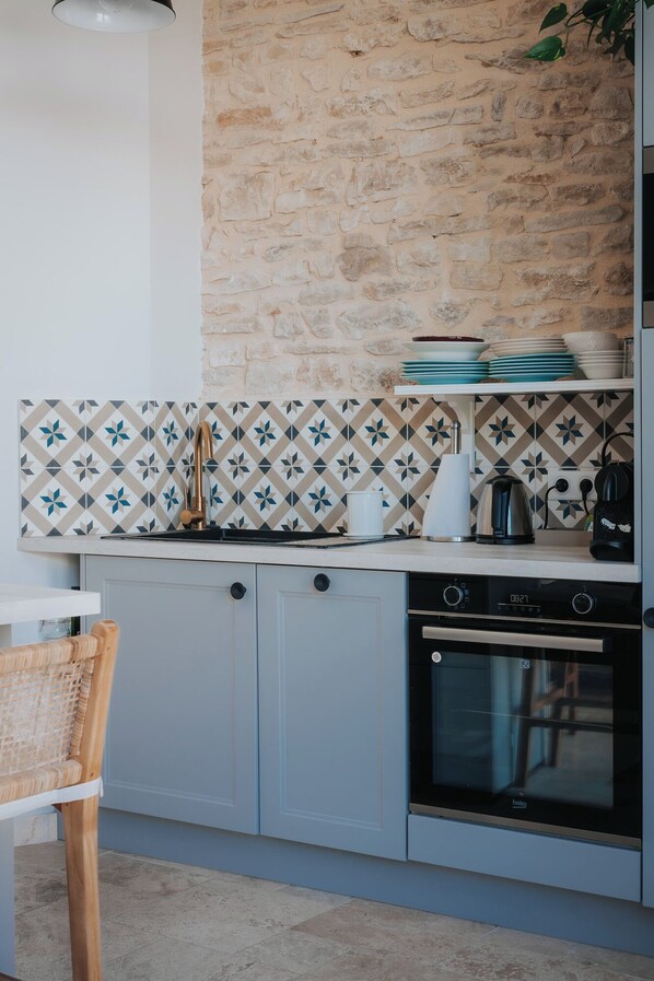 A modern kitchen with a stone wall backsplash, a built-in oven, and a dining area with a wicker chair.