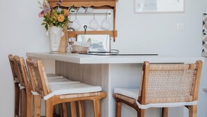 Uma cozinha com uma ilha de madeira, cadeiras brancas e um suporte para panelas suspenso.