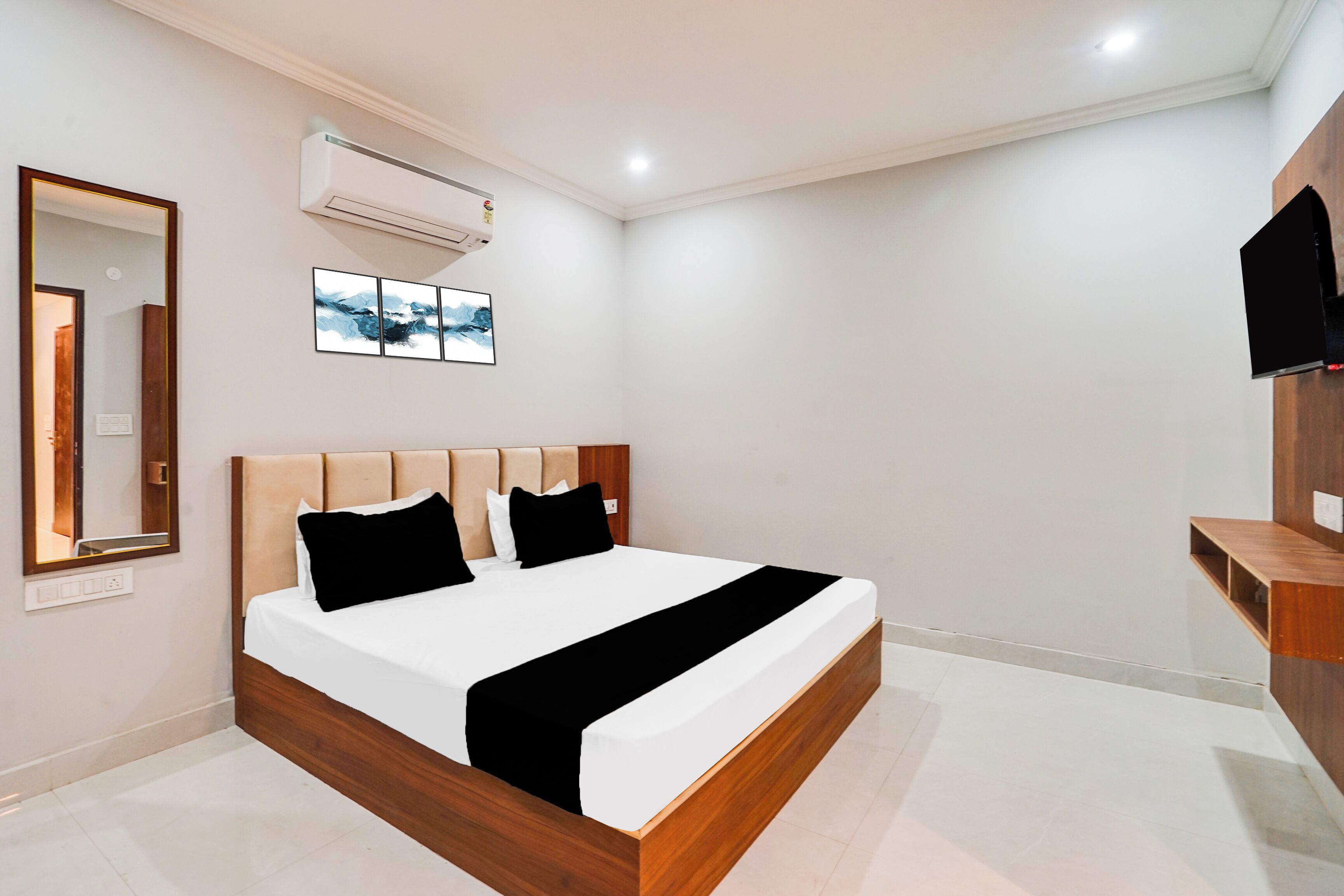 A modern bedroom with a wooden bed frame, white bedding, and a mounted TV.