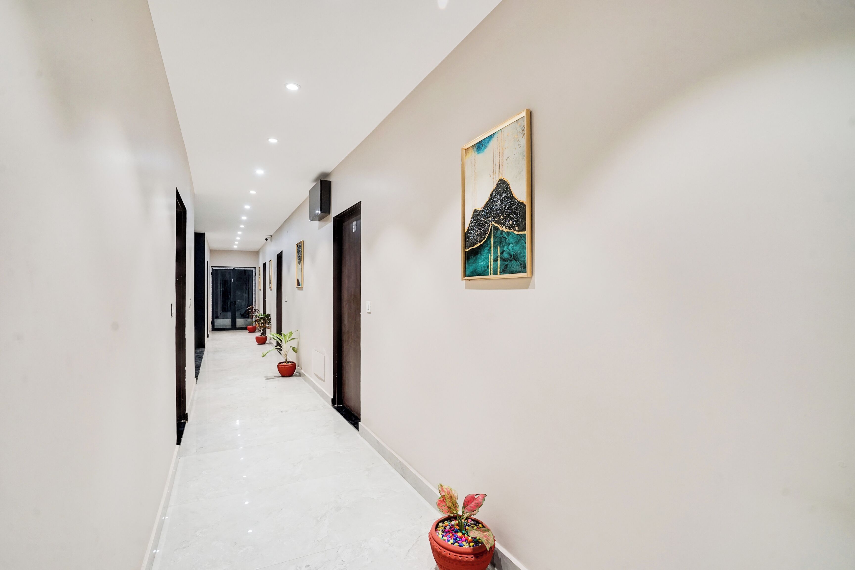A hallway with a white floor, potted plants, and a painting on the wall.