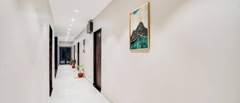 A hallway with a white floor, potted plants, and a painting on the wall.
