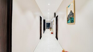 A long, narrow hallway with white walls and a marble floor. There are several doors on either side, and a framed artwork hangs on the right wall. - Hotel Grand Aana Inn (Jaipur)