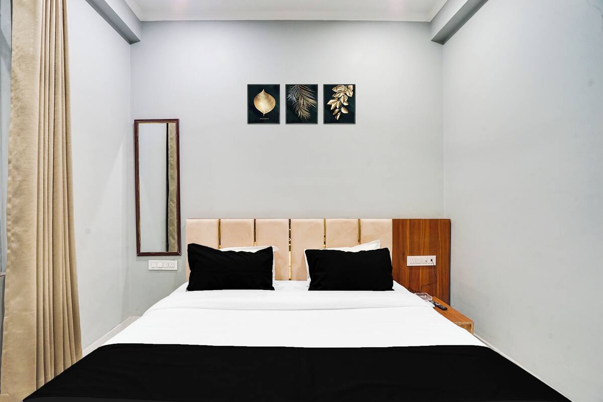 Un dormitorio con cama, dos almohadas negras, cabecera de madera, mesita de noche, espejo y tres obras de arte en la pared.